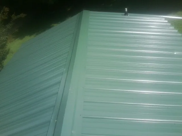 New green metal panels meeting at the ridge of a roof — Flat Roof Repair work by our crew in Clay